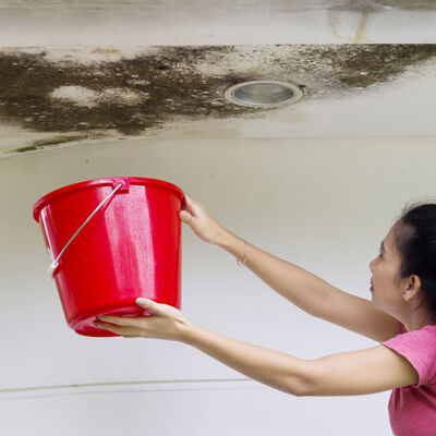 Woman holds a bucket for collecting rainwater from damaged ceiling
